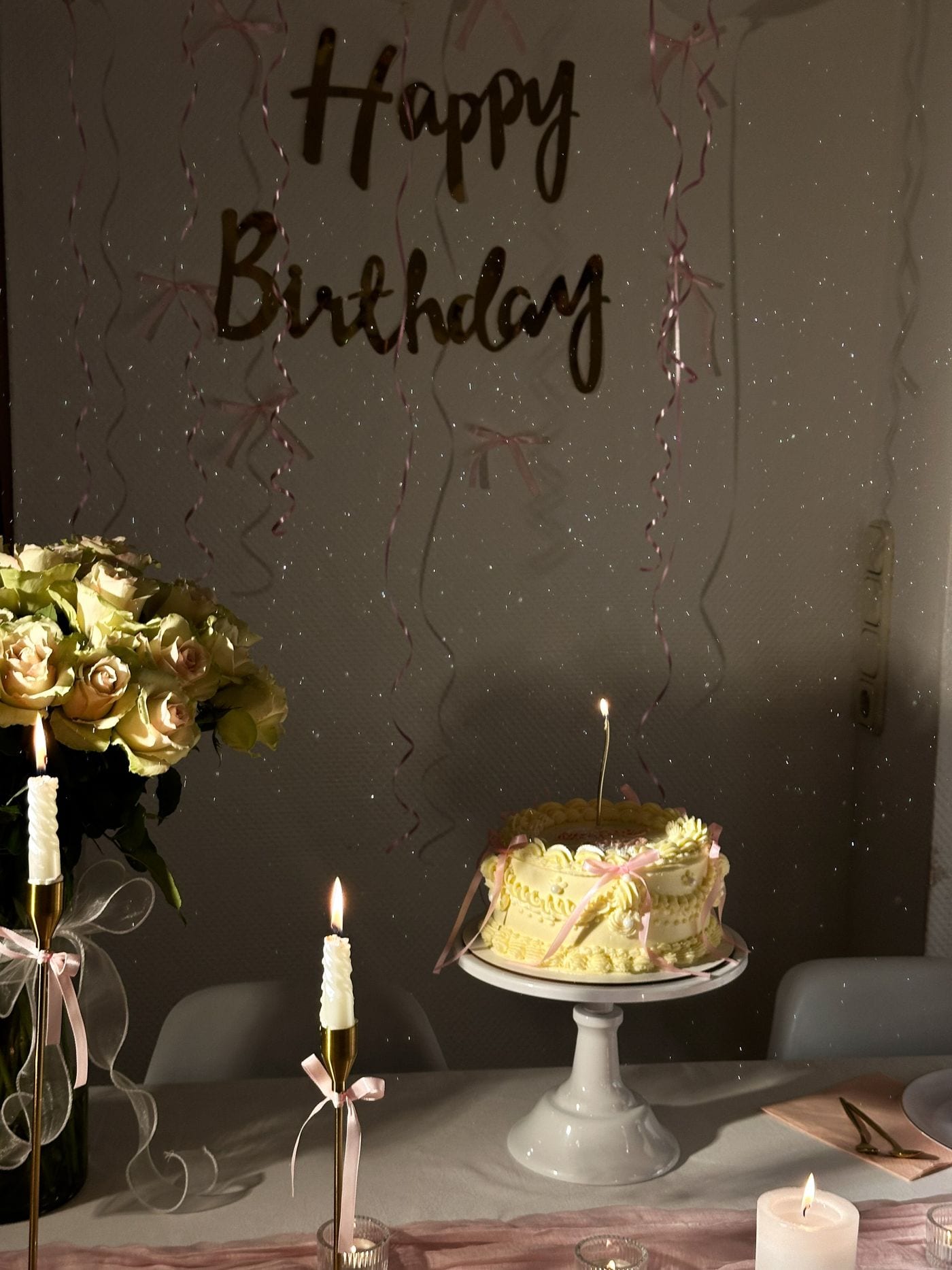 Candlelit celebration table with a ribboned cake, cream roses and slim tapers