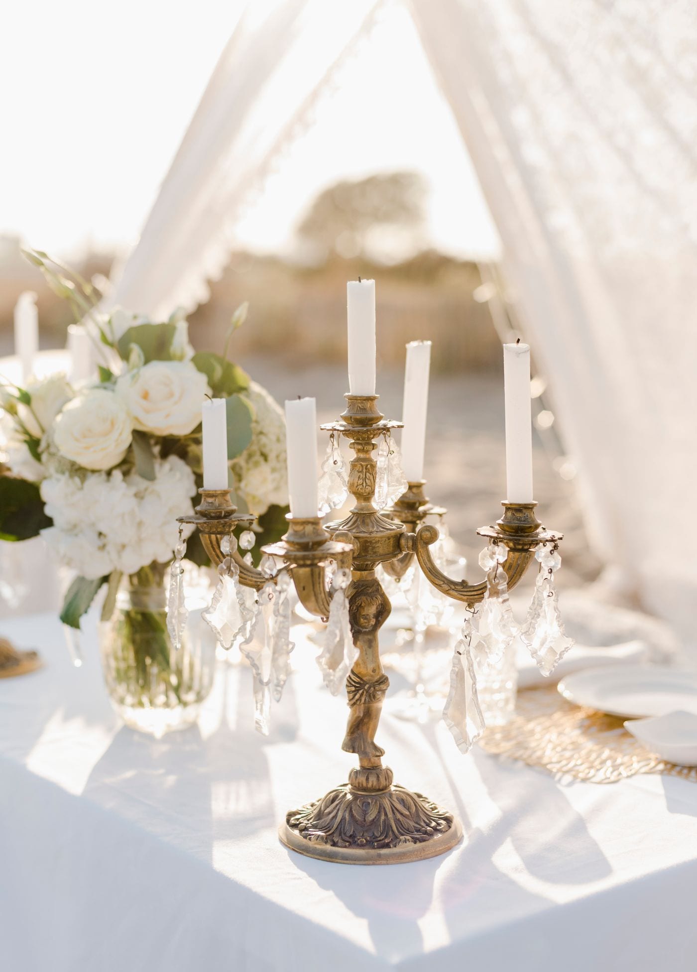 Antique brass candelabra with ivory candles and white roses on a draped table