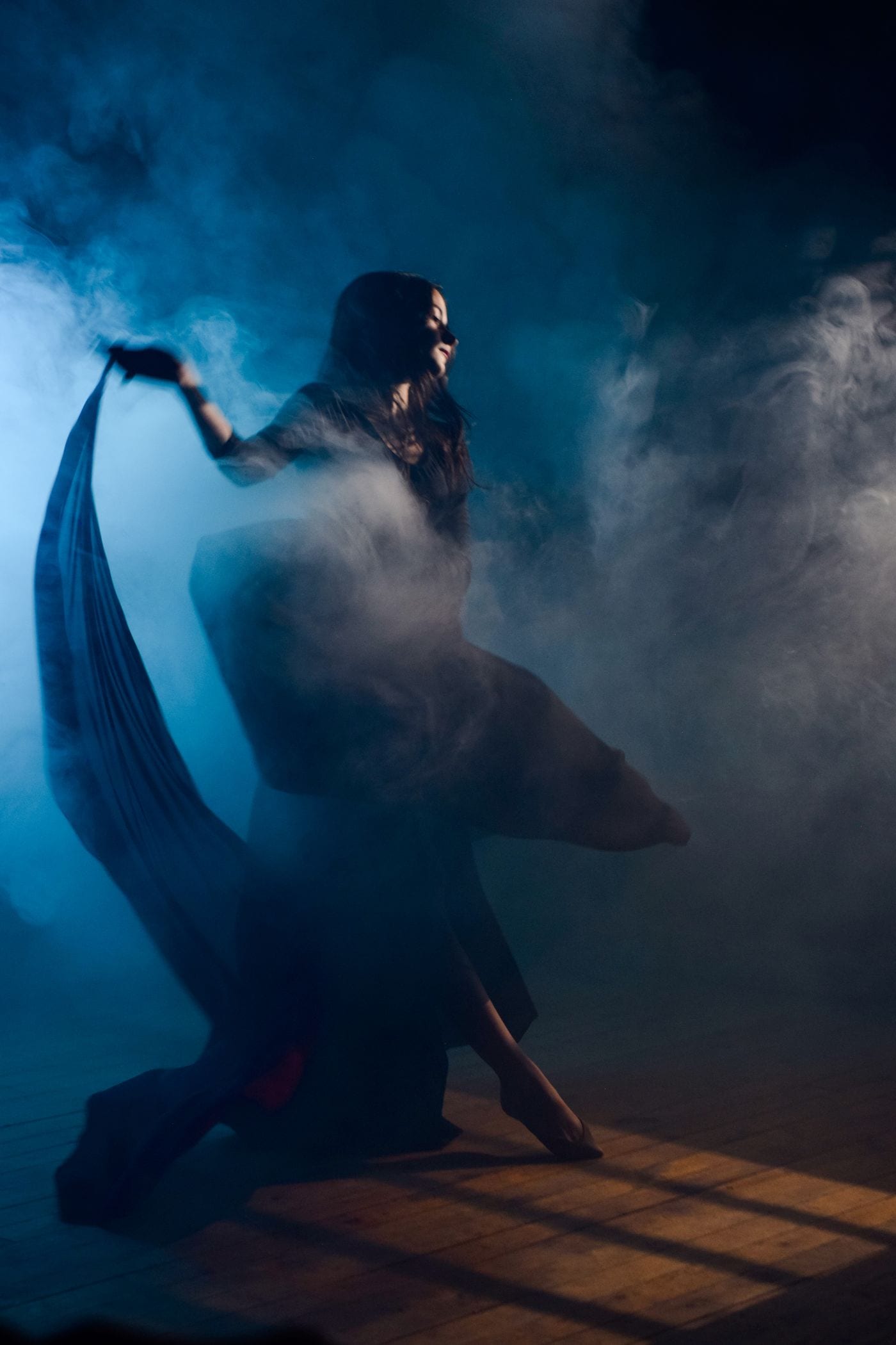 Dancer turning through blue fog, skirt caught in the light
