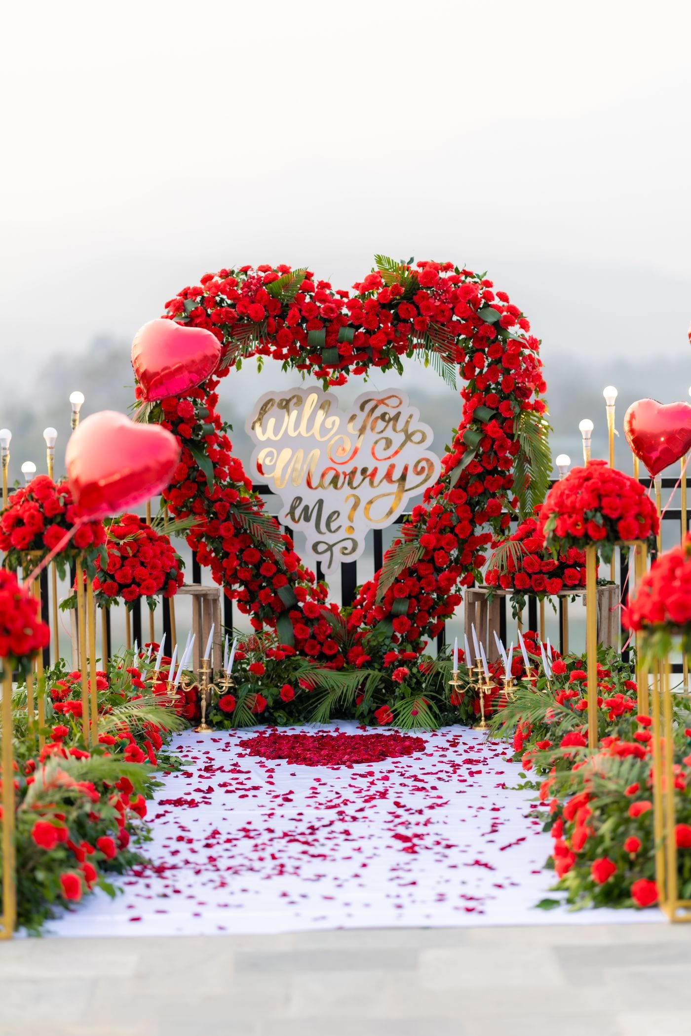Romantic sunset proposal with a rose heart arch, candles and rose petals